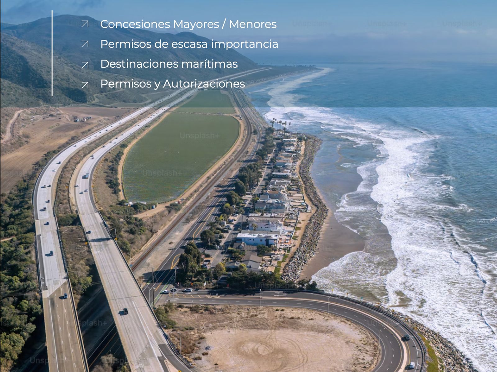 Aerial view of a winding coastal highway beside a sandy beach and blue ocean with a small town along the shore.